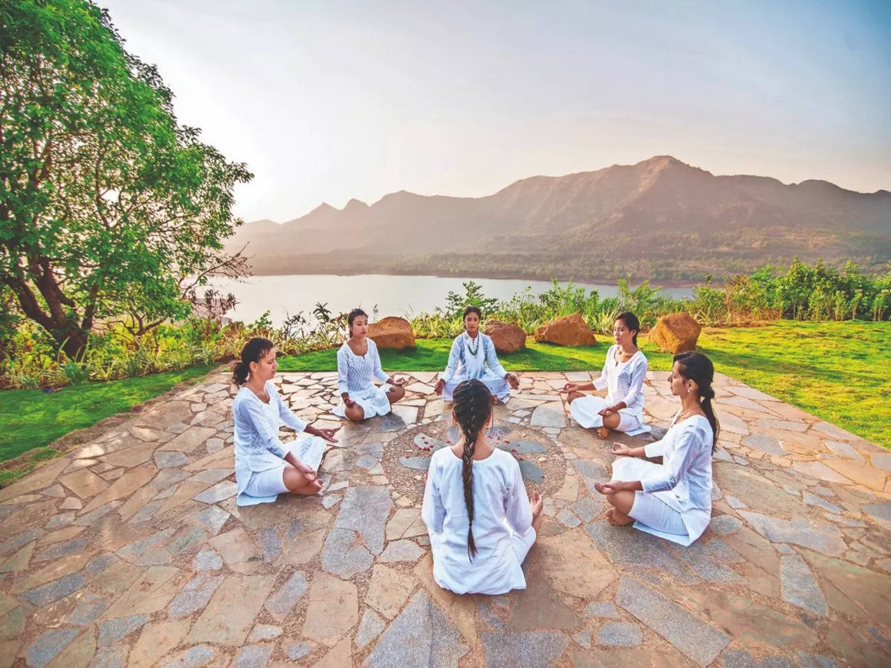 A group meditating outdoors in a serene natural setting.